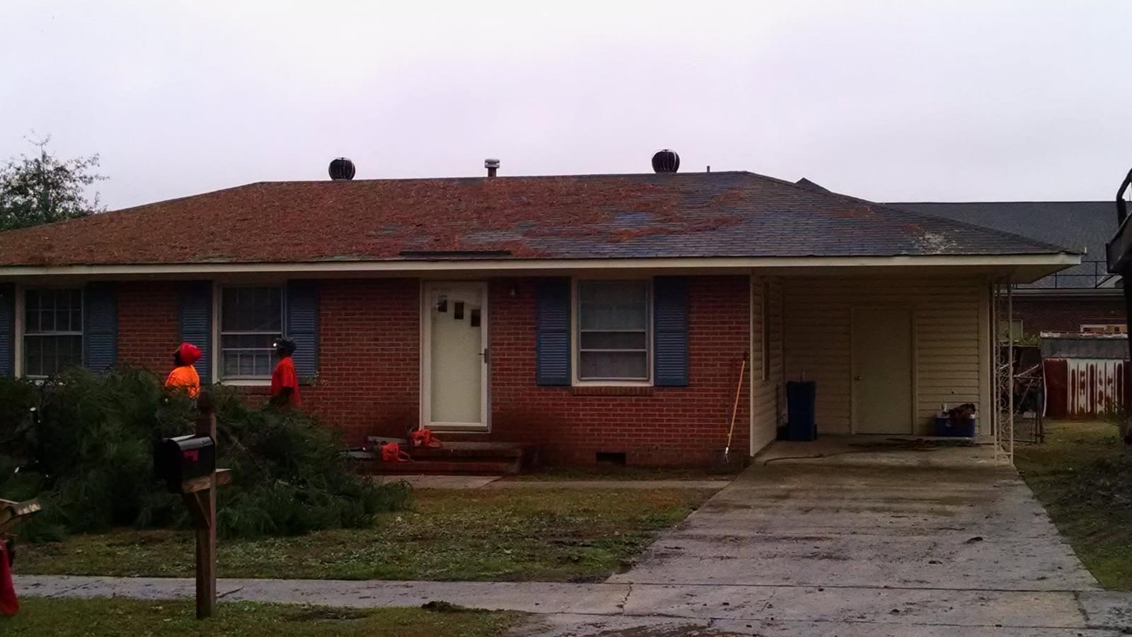 Burks Tree Service crew clearing cut pine limbs in front of a brick ranch home